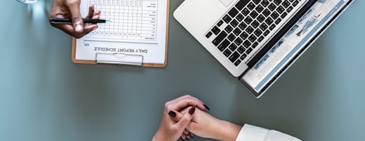 Medical practice management consultants reviewing a daily report and financial data on a laptop.